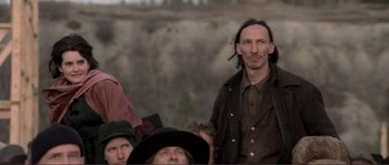 Movie still from “The Claim” (2000), directed by Michael Winterbottom – A man with long hair is standing in front of a group of people; Medium shot, Low angle