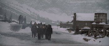 Movie still from “The Claim” (2000), directed by Michael Winterbottom – A group of people are walking in the snow; Extreme Wide shot, High angle