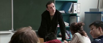Movie still from “The Class” (2008), directed by Laurent Cantet – A man standing in front of a group of people in a classroom; Medium shot, Over the shoulder angle