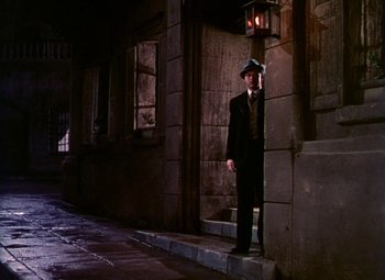 Movie still from “The Climax” (1944), directed by George Waggner – A man in a suit and hat standing in front of a building; Wide shot, Low angle