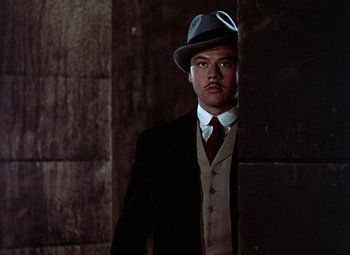 Movie still from “The Climax” (1944), directed by George Waggner – A man in a suit and hat standing in a dark room; Medium shot, Low angle