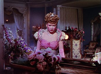 Movie still from “The Climax” (1944), directed by George Waggner – A woman in a pink dress standing in front of a mirror; Medium shot, Low angle