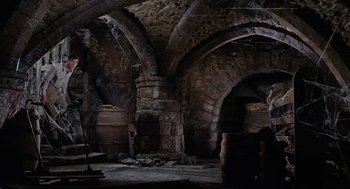 Movie still from “The Collector” (1965), directed by William Wyler – An image of an old stone building with a barrel in the middle of the room; Extreme Wide shot, High angle
