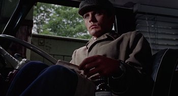 Movie still from “The Collector” (1965), directed by William Wyler – A man sitting in a car reading a newspaper; Close Up shot, Low angle