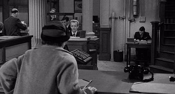 Movie still from “The Collector” (1965), directed by William Wyler – An old photo of a man sitting at a computer desk; Medium shot, Over the shoulder angle