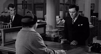 Movie still from “The Collector” (1965), directed by William Wyler – An old photo of a man at a counter with a woman; Medium shot, Over the shoulder angle