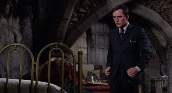 Movie still from “The Collector” (1965), directed by William Wyler – A man in a suit standing in front of a bed; Medium shot, Over the shoulder angle