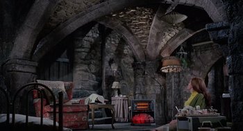 Movie still from “The Collector” (1965), directed by William Wyler – A living room filled with furniture next to an arched stone wall; Wide shot, High angle