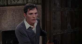 Movie still from “The Collector” (1965), directed by William Wyler – A man in a suit and tie standing next to a wooden door; Medium shot, High angle