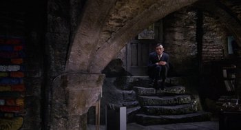 Movie still from “The Collector” (1965), directed by William Wyler – A man sitting on some steps in a building; Wide shot, High angle