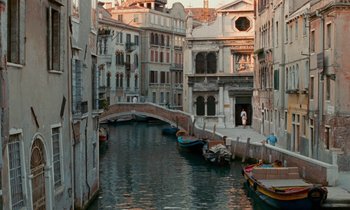 Movie still from “The Comfort of Strangers” (1990), directed by Paul Schrader – A view of a canal in a city with buildings; Extreme Wide shot, High angle