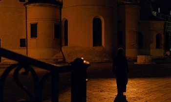 Movie still from “The Comfort of Strangers” (1990), directed by Paul Schrader – A person standing in front of a building at night; Extreme Wide shot, Low angle