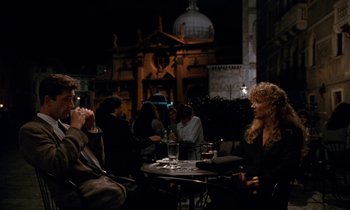 Movie still from “The Comfort of Strangers” (1990), directed by Paul Schrader – A group of people sitting at a table at night; Wide shot, Over the shoulder angle