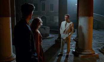 Movie still from “The Comfort of Strangers” (1990), directed by Paul Schrader – A group of people standing around in a building; Wide shot, Over the shoulder angle