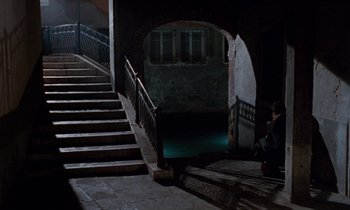 Movie still from “The Comfort of Strangers” (1990), directed by Paul Schrader – A person sitting on a set of stairs at the top of the steps; Extreme Wide shot, High angle