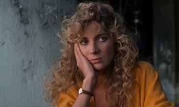 Movie still from “The Comfort of Strangers” (1990), directed by Paul Schrader – A woman with curly hair is leaning against a wall with her hand on her face; Close Up shot, High angle