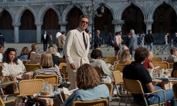 Movie still from “The Comfort of Strangers” (1990), directed by Paul Schrader – A man in a white suit standing in front of a group of people; Wide shot, Over the shoulder angle