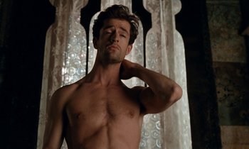 Movie still from “The Comfort of Strangers” (1990), directed by Paul Schrader – A shirtless man standing in front of a window; Medium shot, Overhead angle
