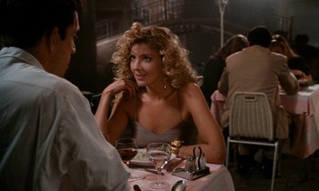 Movie still from “The Comfort of Strangers” (1990), directed by Paul Schrader – A woman sitting at a table with a glass of red wine; Medium shot, Over the shoulder angle