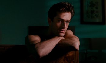 Movie still from “The Comfort of Strangers” (1990), directed by Paul Schrader – A shirtless man leaning on a chair in a dark room; Close Up shot, Low angle