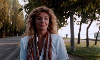 Movie still from “The Comfort of Strangers” (1990), directed by Paul Schrader – A woman standing next to a tree in a park; Close Up shot, Low angle
