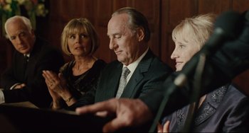 Movie still from “The Company Men” (2010), directed by John Wells – A man and two women are sitting in front of a microphone; Close Up shot, Over the shoulder angle