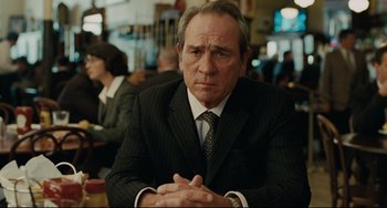 Movie still from “The Company Men” (2010), directed by John Wells – A man in a suit and tie sitting at a table with his hands crossed; Close Up shot, Over the shoulder angle
