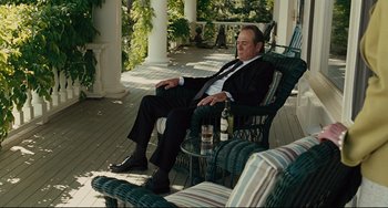 Movie still from “The Company Men” (2010), directed by John Wells – A man in a suit and tie sitting in a chair with a bottle of beer; Medium shot, High angle