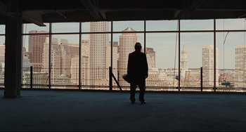 Movie still from “The Company Men” (2010), directed by John Wells – A man standing in front of a large window with a view of a city; Extreme Wide shot, Low angle