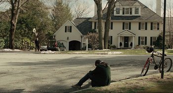 Movie still from “The Company Men” (2010), directed by John Wells – A man sitting on the side of the road in front of a house; Extreme Wide shot, High angle