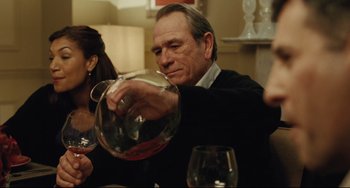 Movie still from “The Company Men” (2010), directed by John Wells – A man pouring wine into a glass at a party; Medium shot, Over the shoulder angle