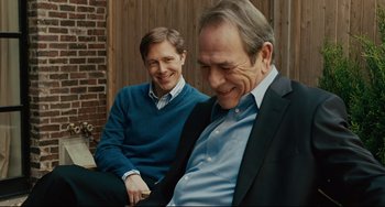 Movie still from “The Company Men” (2010), directed by John Wells – Two men sitting next to each other in front of a brick wall; Medium shot, Over the shoulder angle