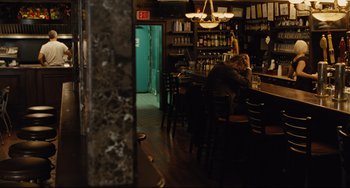 Movie still from “The Company Men” (2010), directed by John Wells – A man sitting at a table in front of a bottle of wine; Wide shot, Over the shoulder angle