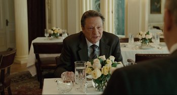 Movie still from “The Company Men” (2010), directed by John Wells – An older man sitting at a table with a vase of flowers; Medium shot, Over the shoulder angle