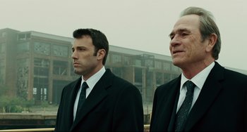 Movie still from “The Company Men” (2010), directed by John Wells – Two men in suits standing next to each other in front of a building; Medium shot, Low angle