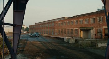 Movie still from “The Company Men” (2010), directed by John Wells – An old factory building with cars parked in front of it; Extreme Wide shot, Low angle