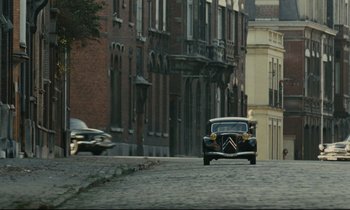 Movie still from “The Confession” (1970), directed by Costa-Gavras – An old car driving down a street past a building; Extreme Wide shot, High angle