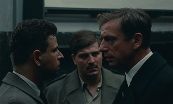 Movie still from “The Confession” (1970), directed by Costa-Gavras – A group of men standing next to each other in a room; Close Up shot, Over the shoulder angle