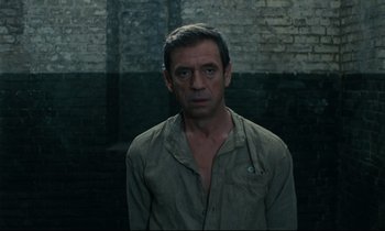 Movie still from “The Confession” (1970), directed by Costa-Gavras – A man standing in front of a brick wall; Medium shot, Low angle