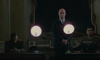 Movie still from “The Confession” (1970), directed by Costa-Gavras – A man standing in front of two lamps in a dark room; Medium shot, Low angle