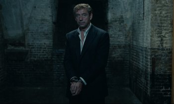 Movie still from “The Confession” (1970), directed by Costa-Gavras – A man in a black suit standing in a dark room; Medium shot, Low angle