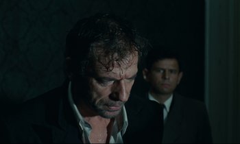 Movie still from “The Confession” (1970), directed by Costa-Gavras – A man in a suit and tie standing next to another man in a suit and tie; Close Up shot, Over the shoulder angle