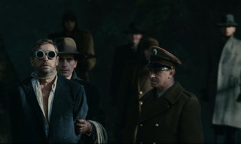 Movie still from “The Confession” (1970), directed by Costa-Gavras – A group of men in hats and coats standing next to each other; Medium shot, Over the shoulder angle