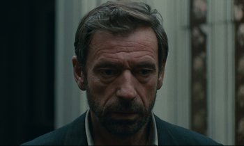 Movie still from “The Confession” (1970), directed by Costa-Gavras – A person wearing a suit and tie; Close Up shot, Low angle