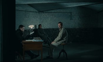 Movie still from “The Confession” (1970), directed by Costa-Gavras – A group of men sitting at a table in a dark room; Wide shot, High angle