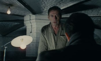 Movie still from “The Confession” (1970), directed by Costa-Gavras – A man standing next to another man in a room; Medium shot, Over the shoulder angle