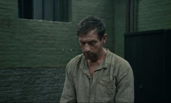 Movie still from “The Confession” (1970), directed by Costa-Gavras – A man in a brown shirt is looking down at the ground; Medium shot, Over the shoulder angle