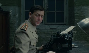 Movie still from “The Confession” (1970), directed by Costa-Gavras – A man in a military uniform sitting in front of a machine; Medium shot, Low angle