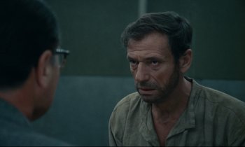 Movie still from “The Confession” (1970), directed by Costa-Gavras – A person wearing glasses and looking at another person; Close Up shot, Over the shoulder angle