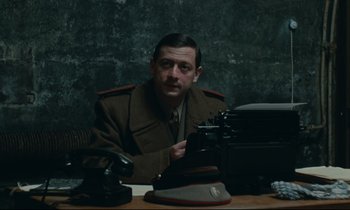 Movie still from “The Confession” (1970), directed by Costa-Gavras – A man sitting at a table with a typewriter; Medium shot, High angle